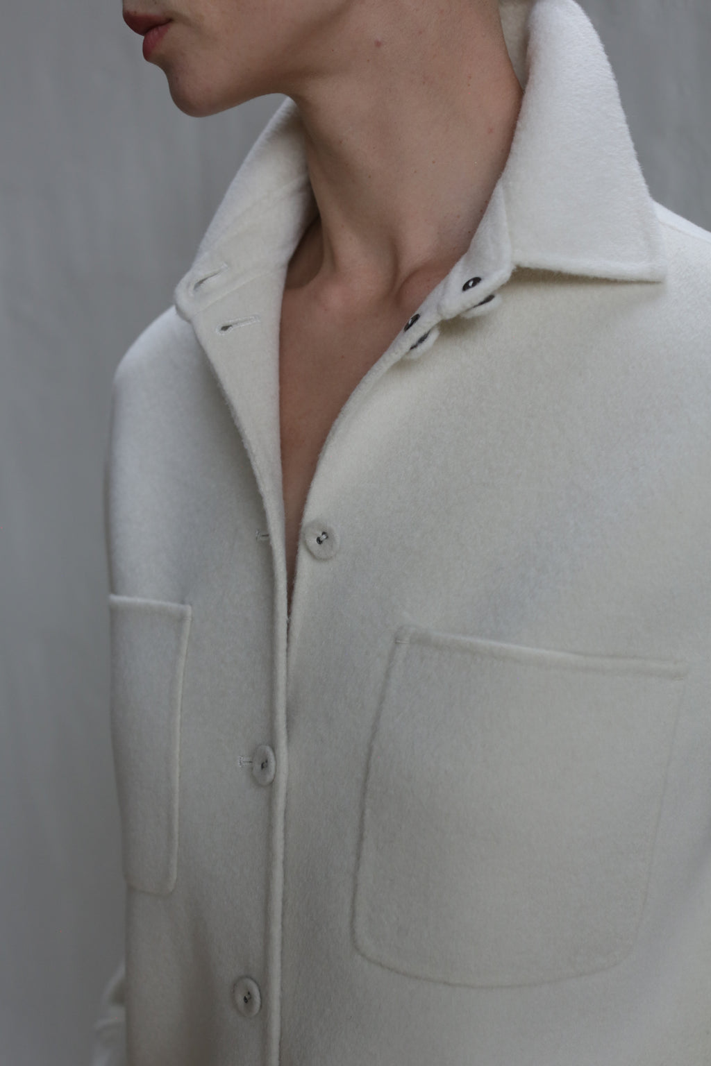 A person wears the Studio Shirt | Undyed—an off-white, button-up fleece jacket with large chest pockets and a turned-up collar—shown from shoulders to just below the chin against a neutral background.