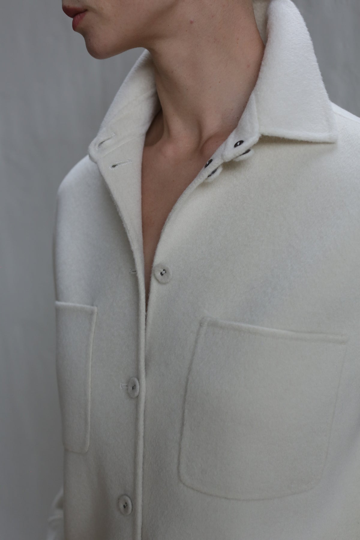 A person wears the Studio Shirt | Undyed—an off-white, button-up fleece jacket with large chest pockets and a turned-up collar—shown from shoulders to just below the chin against a neutral background.