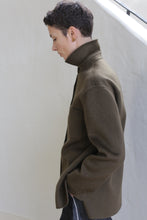 Load image into Gallery viewer, A person with short dark hair stands in profile against a light background, looking down with one hand in their pocket, wearing the Studio Shirt in Olive.