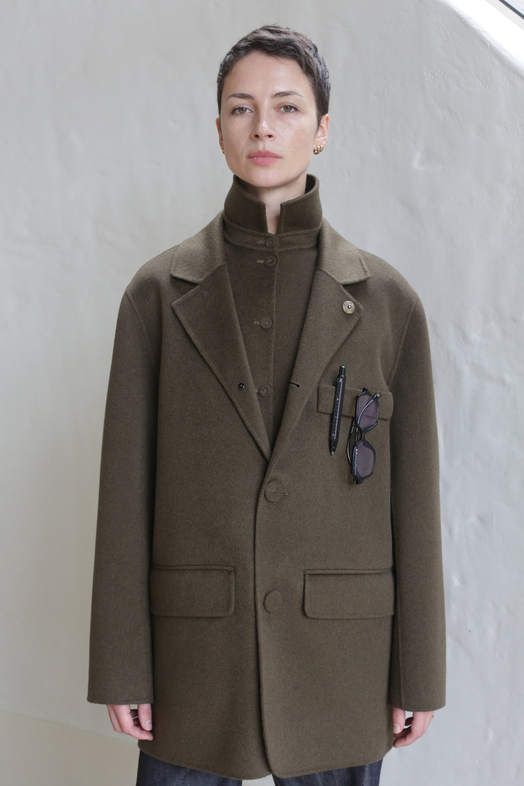 A woman wearing the Sculptor's Jacket in Olive with sunglasses in her pocket.