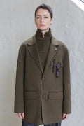 A woman wearing the Sculptor's Jacket in Olive with sunglasses in her pocket.