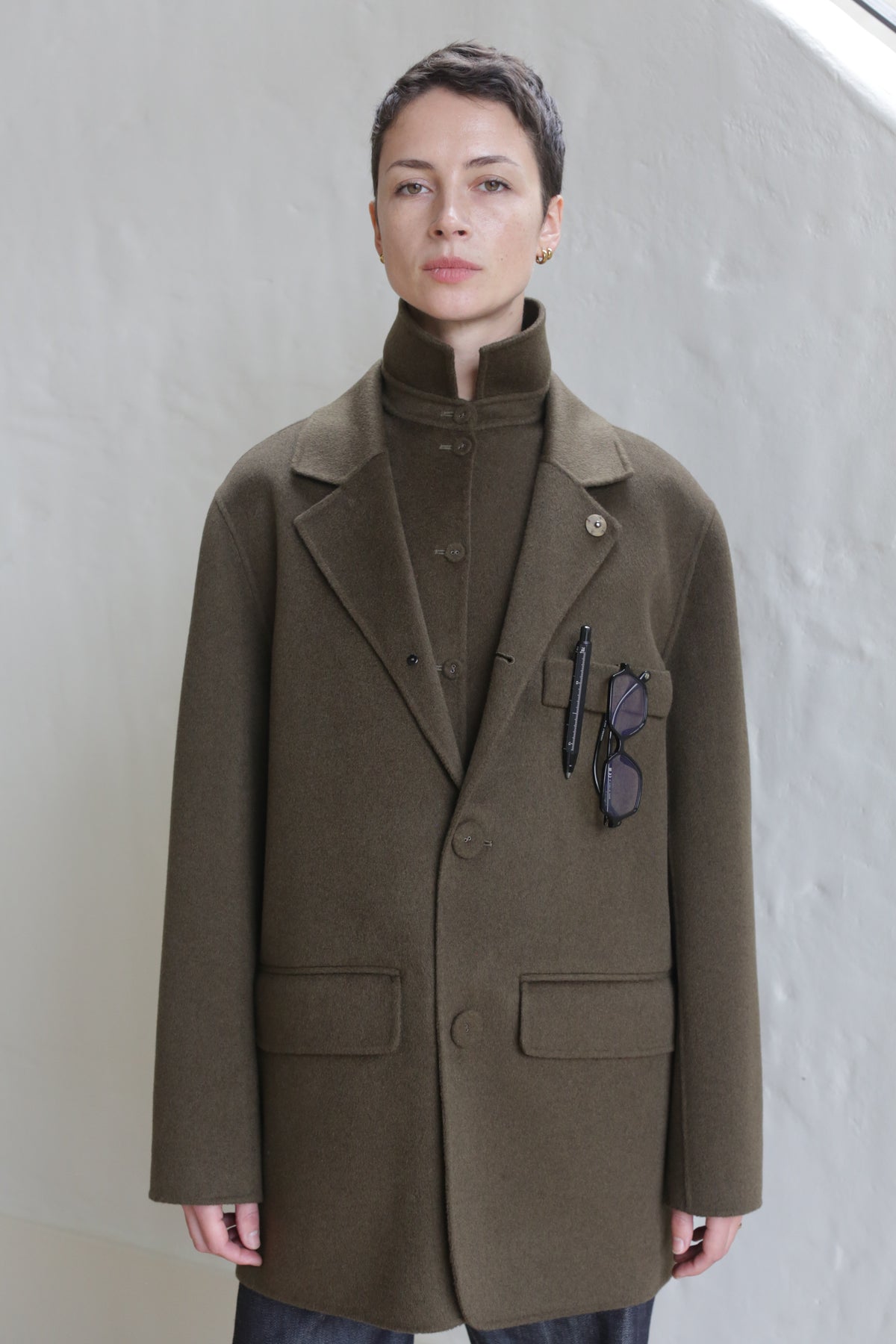 A woman wearing the Sculptor's Jacket in Olive with sunglasses in her pocket.