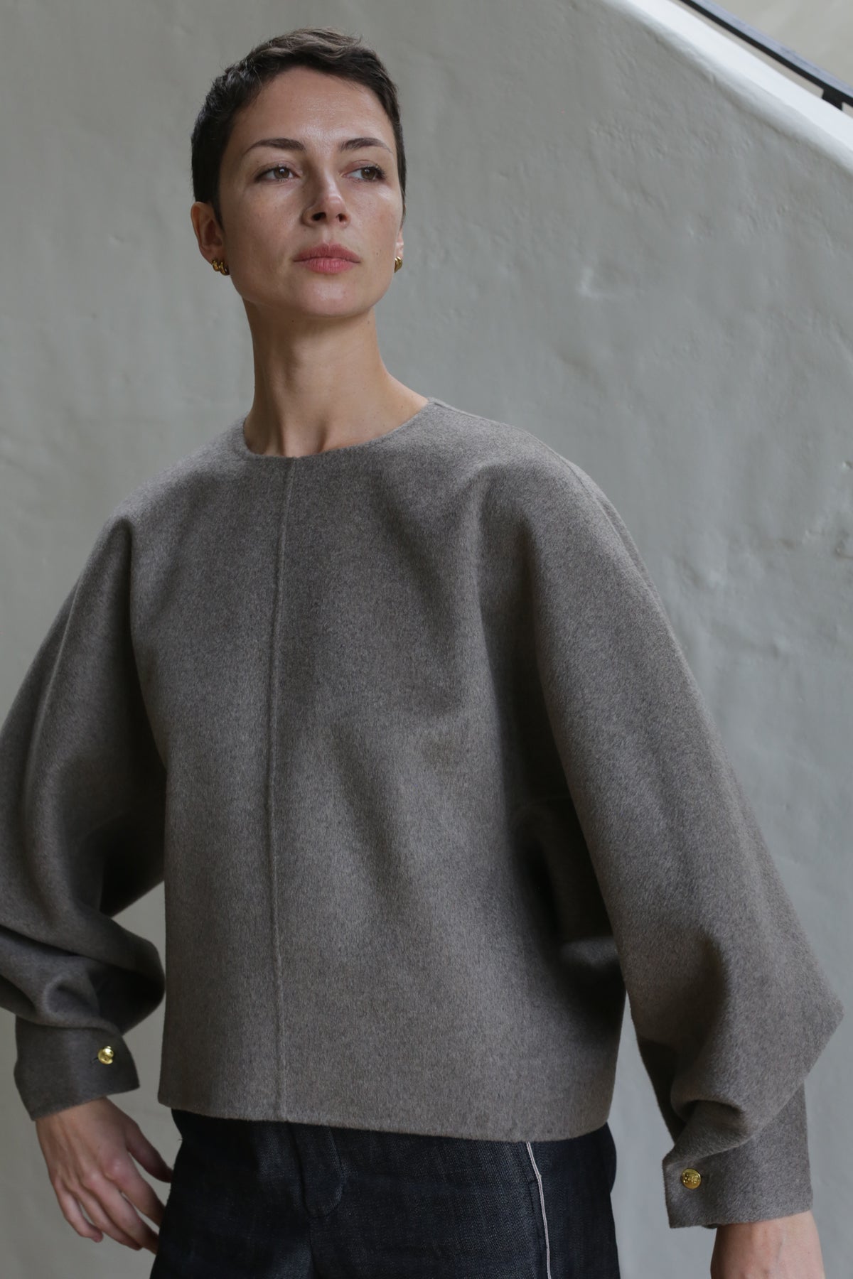 A woman with short hair wearing the Cocoon coat in undyed natural.