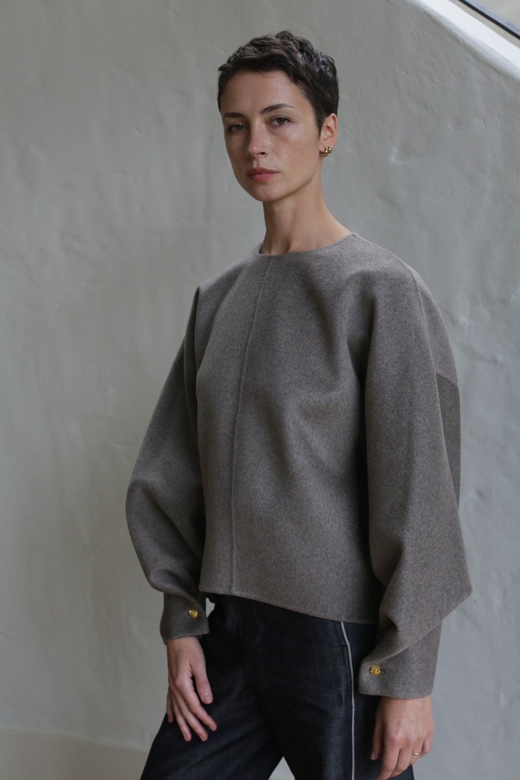 A woman with short hair wears the Cocoon sweater in undyed natural.