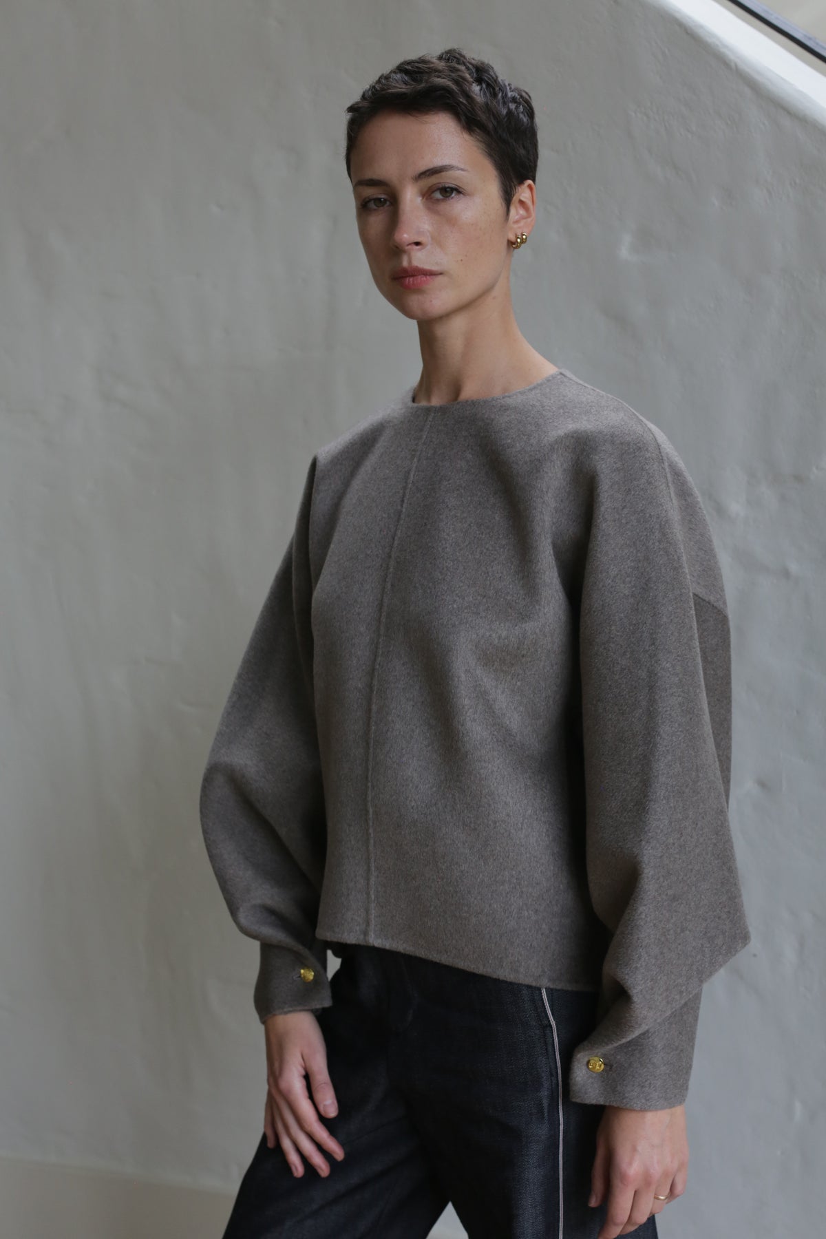 A woman with short hair wears the Cocoon sweater in undyed natural.