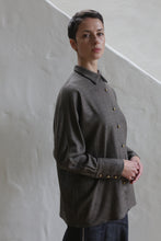 Load image into Gallery viewer, A woman with short brown hair stands in front of a light textured wall, wearing the Work Shirt | Taupe and dark pants, gazing slightly to the side with a neutral expression.