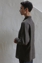 Load image into Gallery viewer, A person with short dark hair, wearing the Work Shirt in Taupe, stands sideways against a light-colored textured wall and looks thoughtfully into the distance.