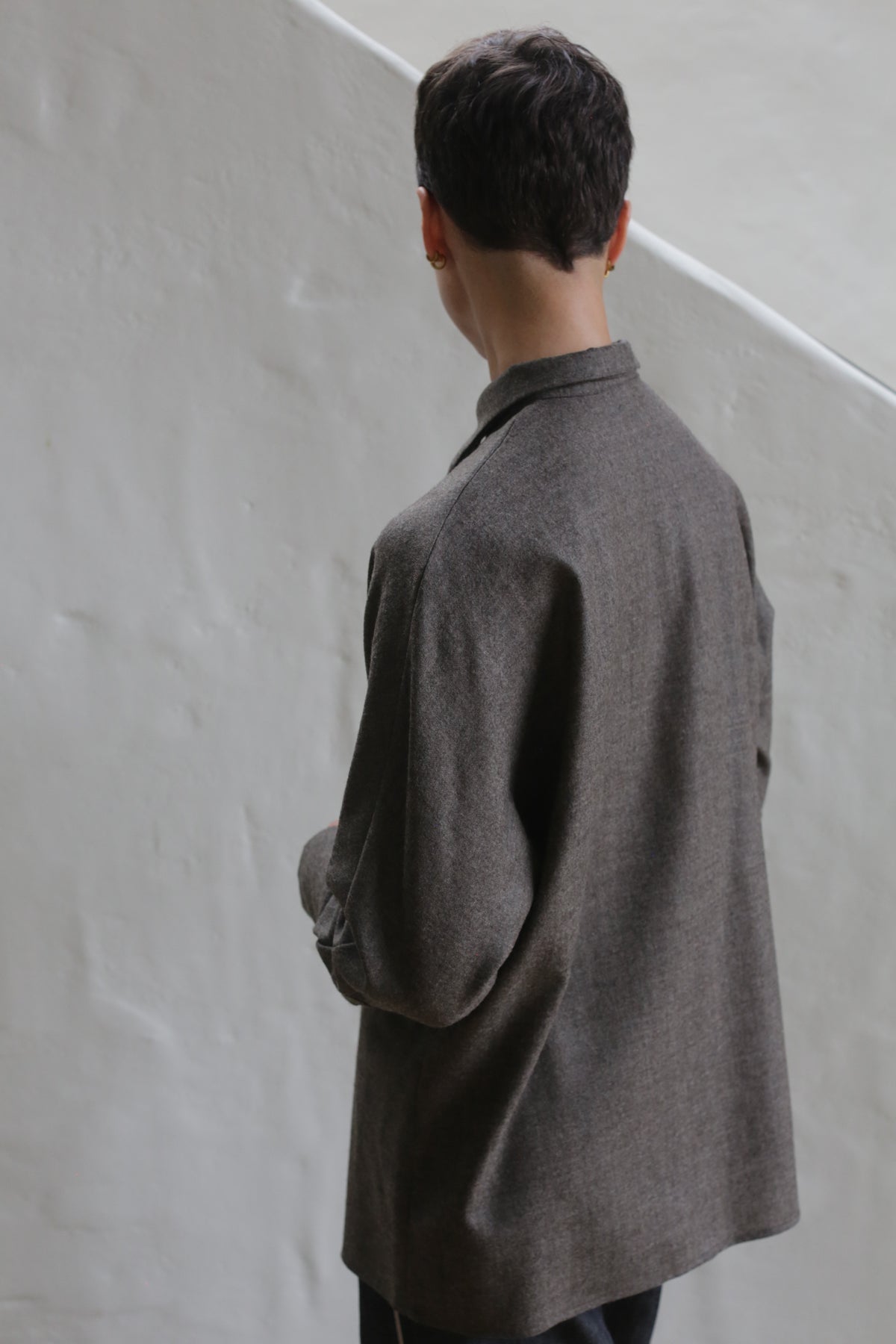 A person wearing the Work Shirt in Taupe stands in front of a white wall.