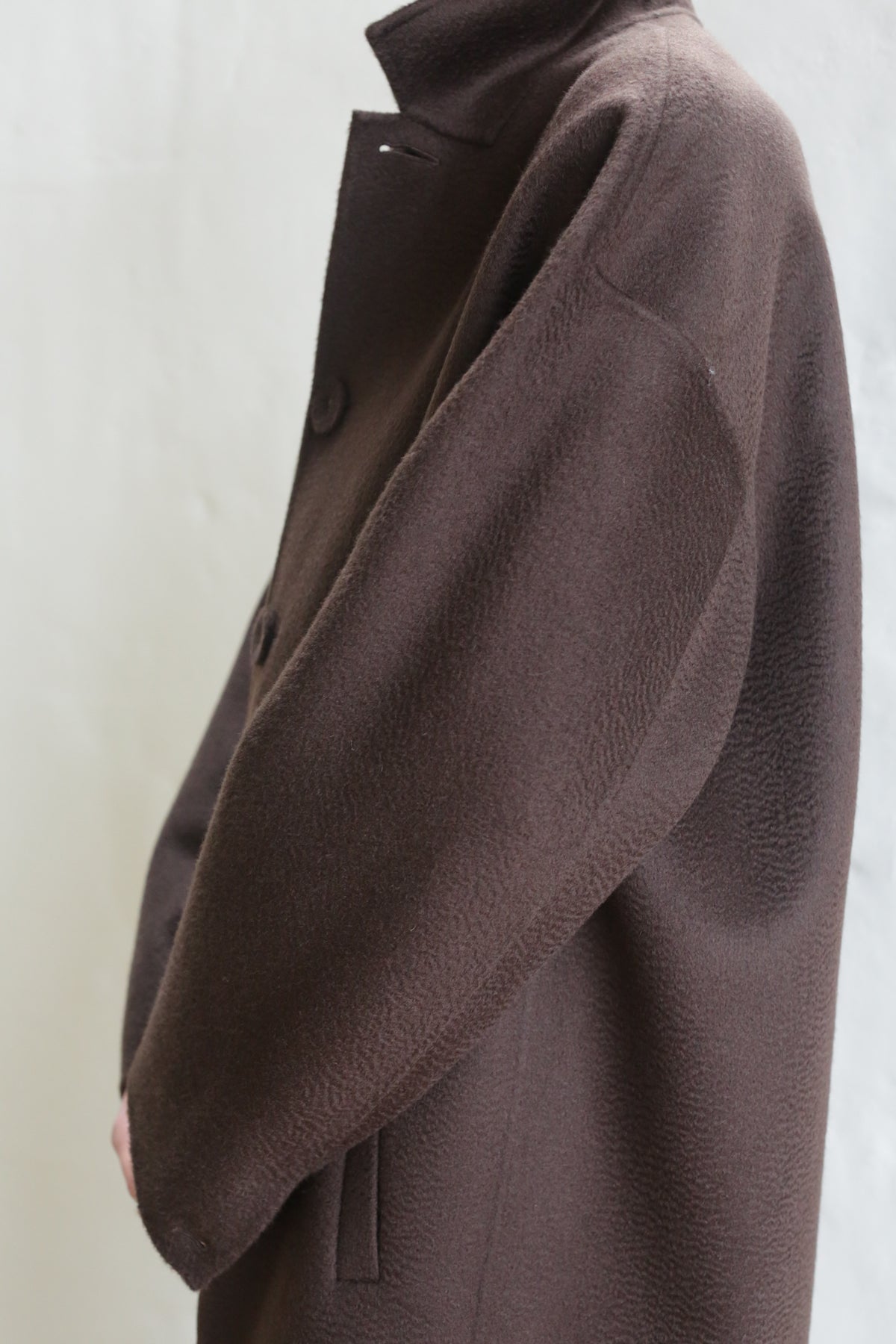A person wears the Men's Coat | Watermark Brown, an oversized, textured brown coat with long, loose sleeves and large buttons, standing against a light background. The person's face is not visible.