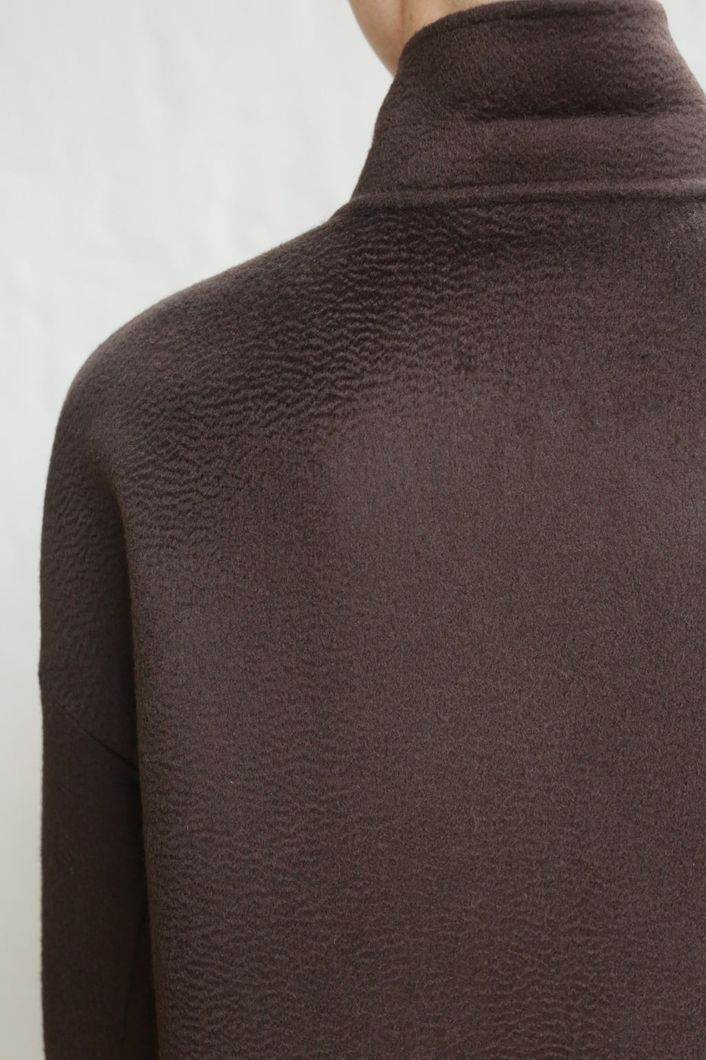 Close-up of a person wearing the Men's Coat | Watermark Double Face Cashmere Brown, featuring a high-neck and textured dark brown double face cashmere, shown from the back and shoulders against a plain light background.