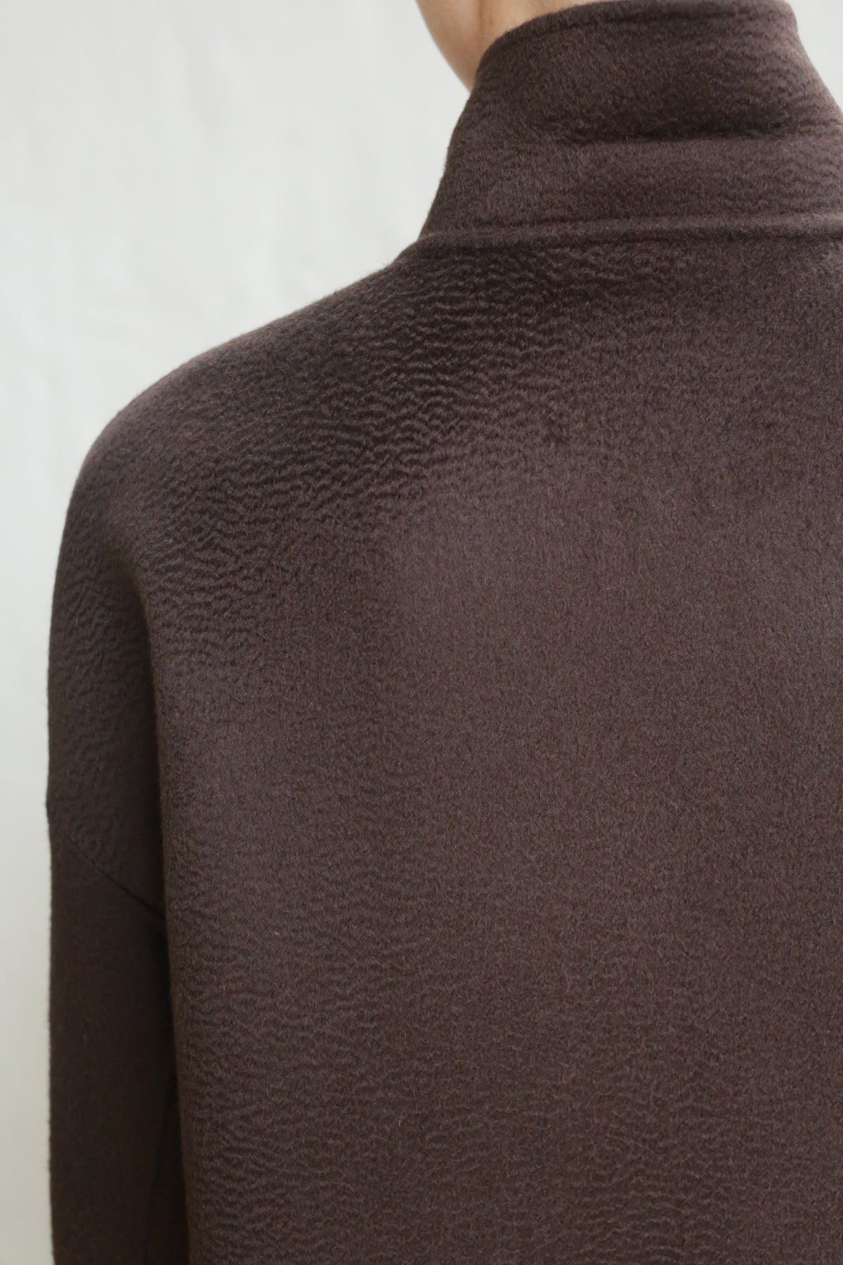 Close-up of a person wearing the Men's Coat | Watermark Double Face Cashmere Brown, featuring a high-neck and textured dark brown double face cashmere, shown from the back and shoulders against a plain light background.