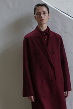 Load image into Gallery viewer, A person with short hair stands against a light wall, wearing the Doublebreasted Coat | Watermark Burgundy over a matching shirt.