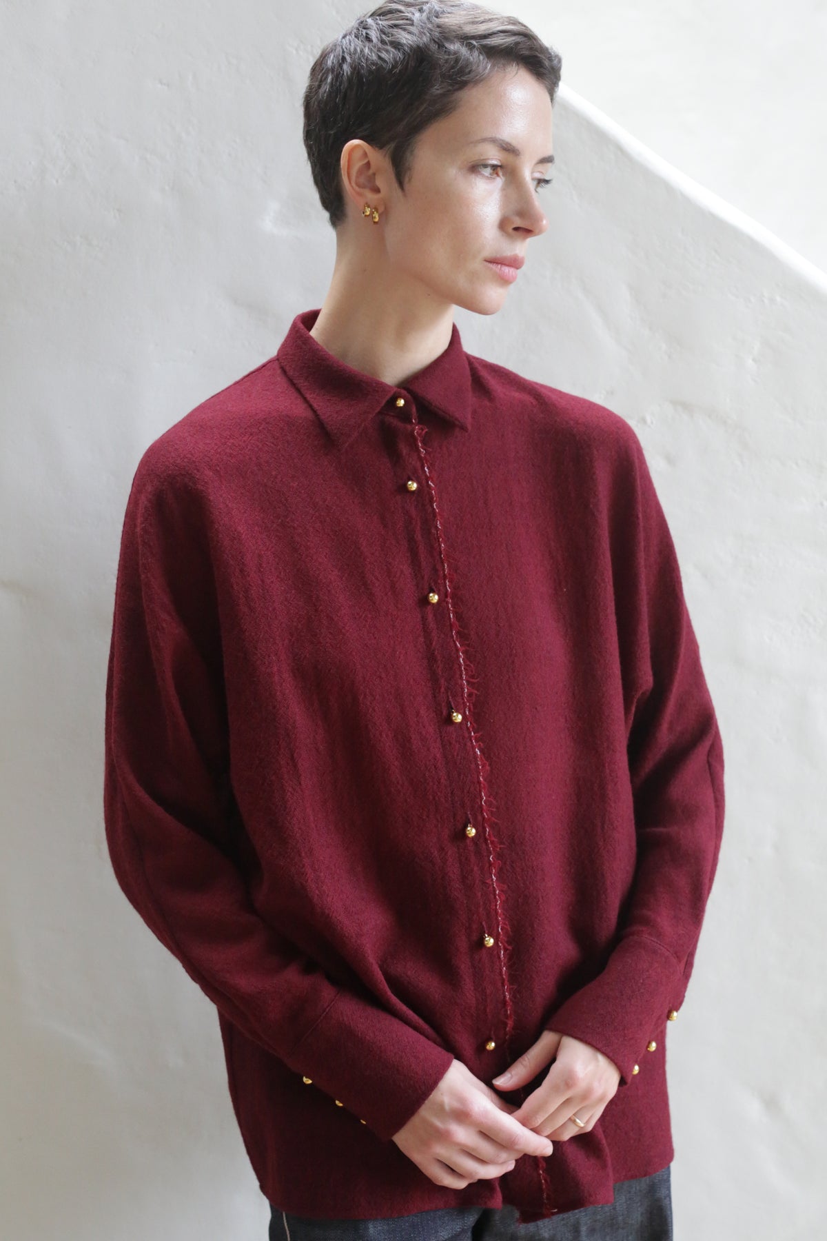 A person with short brown hair, wearing the Work Shirt | Burgundy, stands against a light wall, looking to the side with a neutral expression.