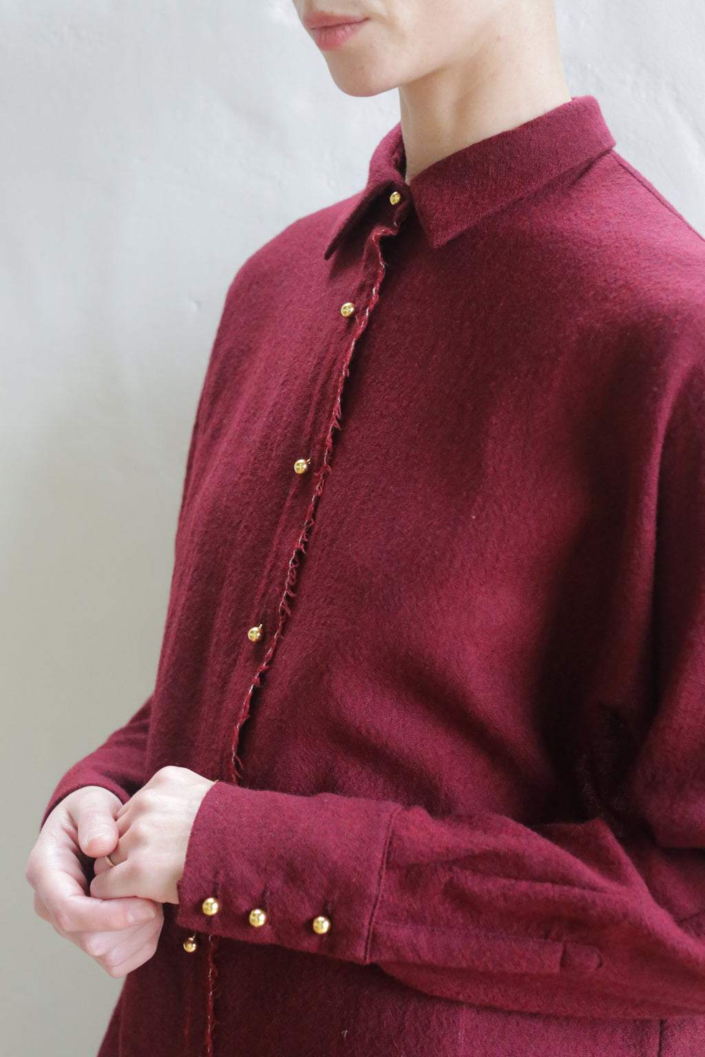 Someone wears the Work Shirt | Burgundy, a long-sleeved shirt with gold buttons on the front and cuffs, standing against a light background. Their face is partially out of frame.