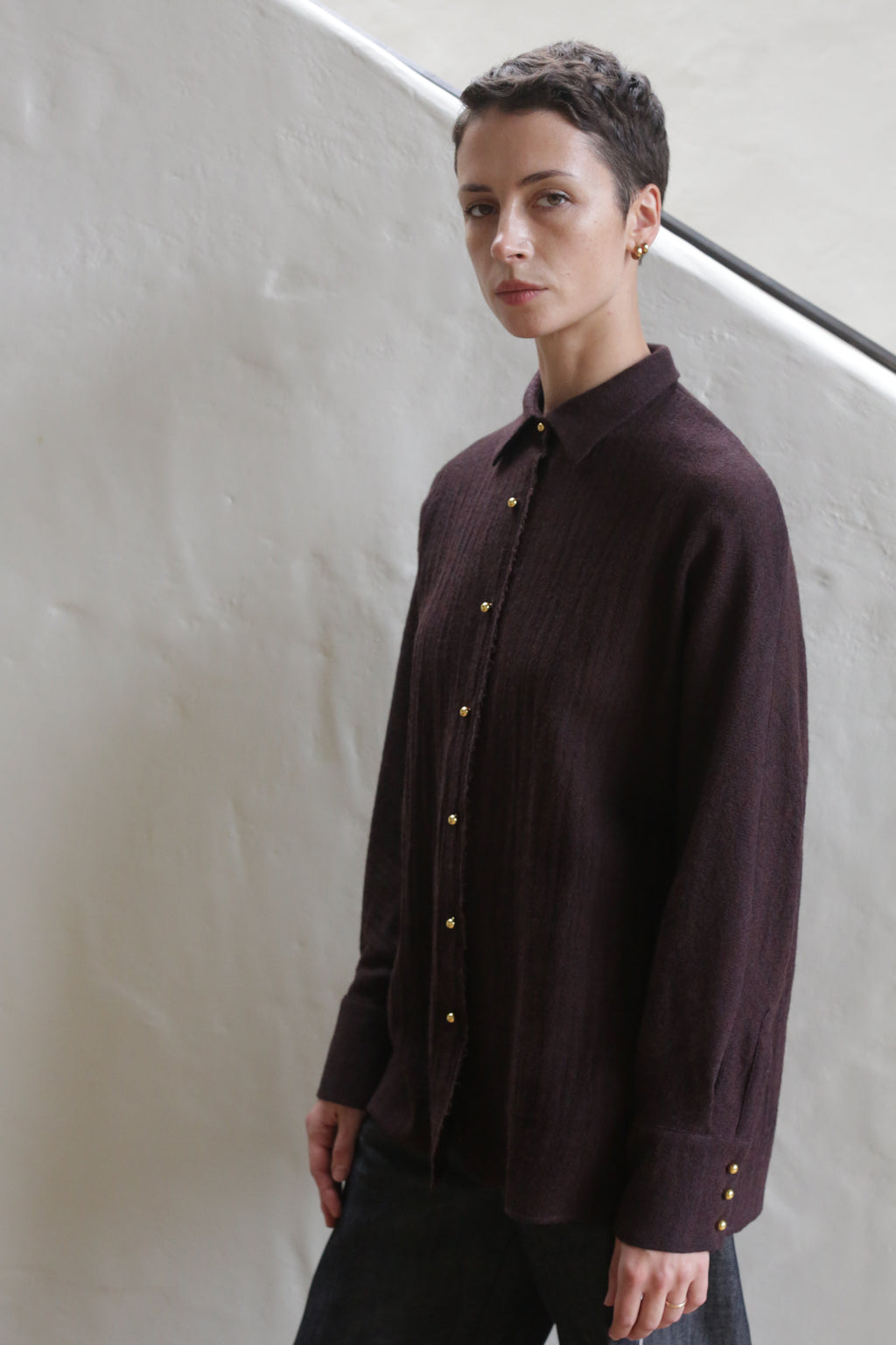 A woman wearing the Work Shirt in Aubergine stands on a staircase.