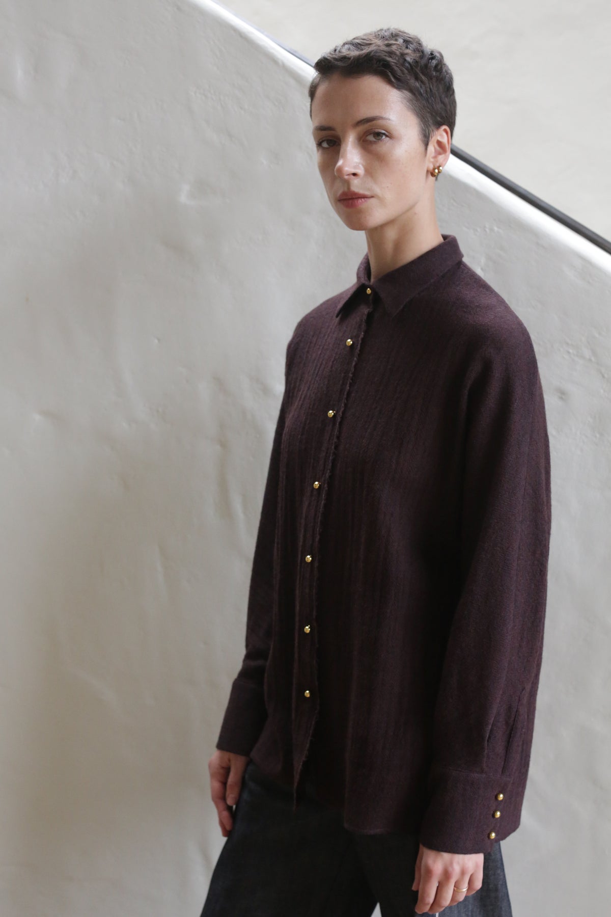 A woman wearing the Work Shirt in Aubergine stands on a staircase.