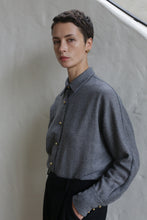 Load image into Gallery viewer, A person with short dark hair wears the Work Shirt | Grey and black pants, standing against a light textured wall, calmly looking at the camera with one hand in their pocket.