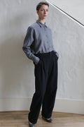 A man wearing Cashmere Pleated Trousers stands with his hands in his pockets.
