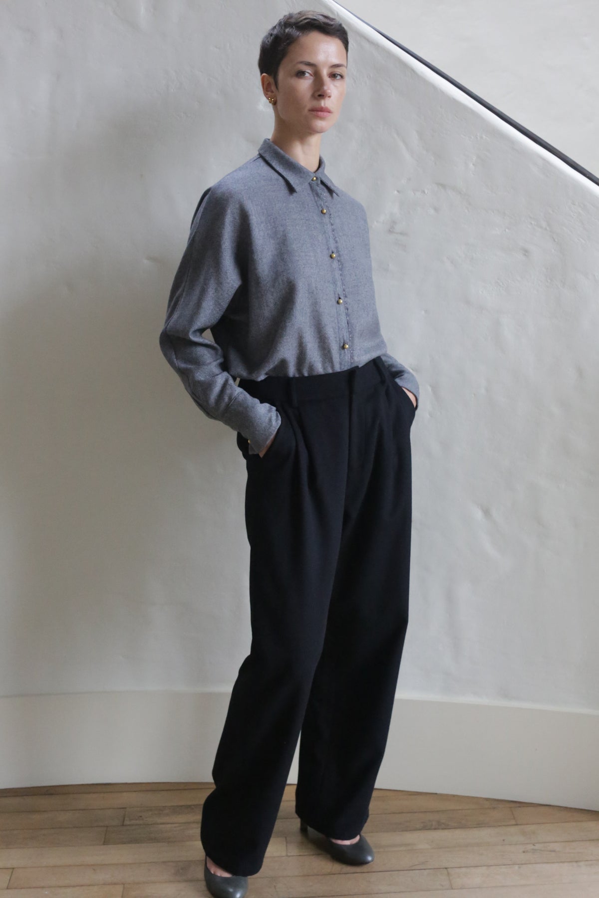 A man wearing Cashmere Pleated Trousers stands with his hands in his pockets.