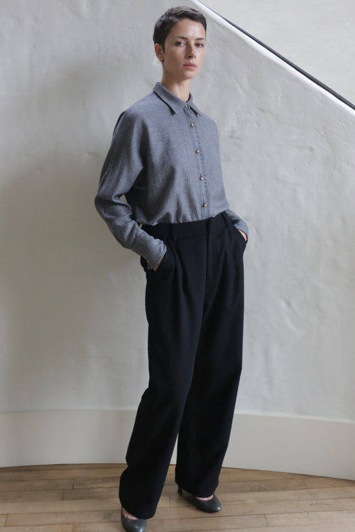 A man wearing Cashmere Pleated Trousers stands with his hands in his pockets.