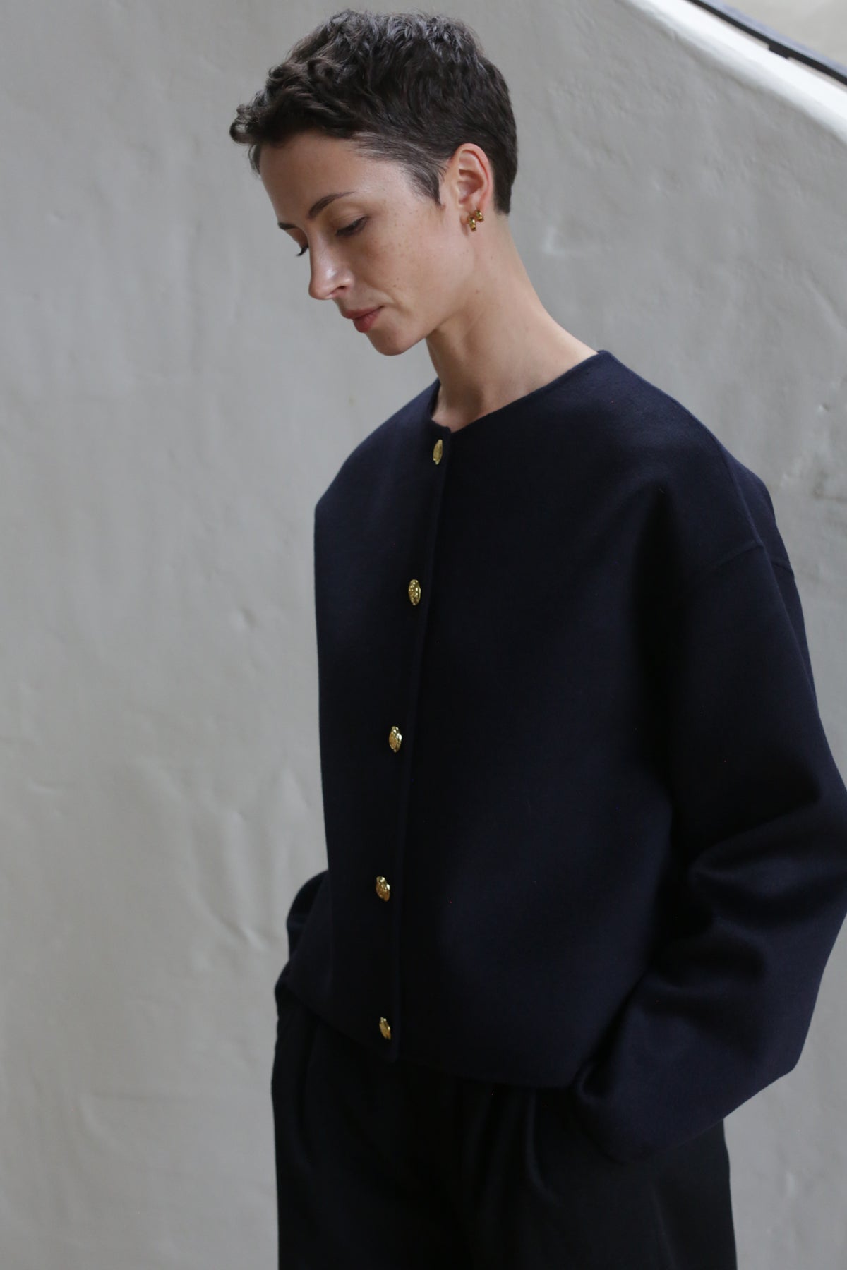 A woman with short hair wearing the Cocoon Jacket in navy.