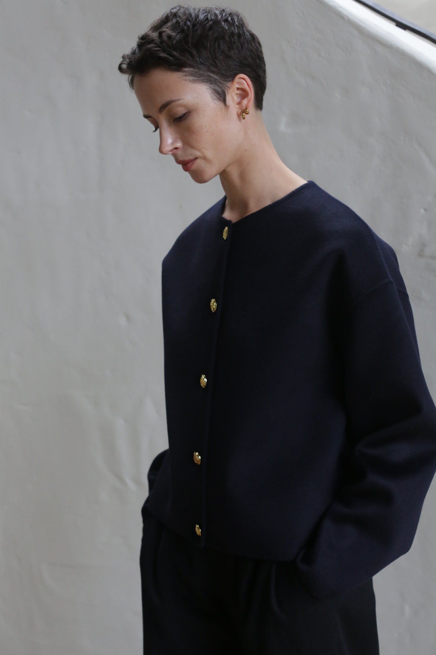 A woman with short hair wearing the Cocoon Jacket in navy.