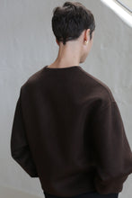 Load image into Gallery viewer, A person with short dark hair models the Cocoon Jacket in Watermark Brown, standing with their back to the camera against a light-colored background.