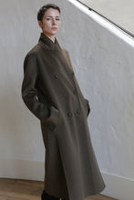 Load image into Gallery viewer, A person wearing the Doublebreasted Coat in Olive.