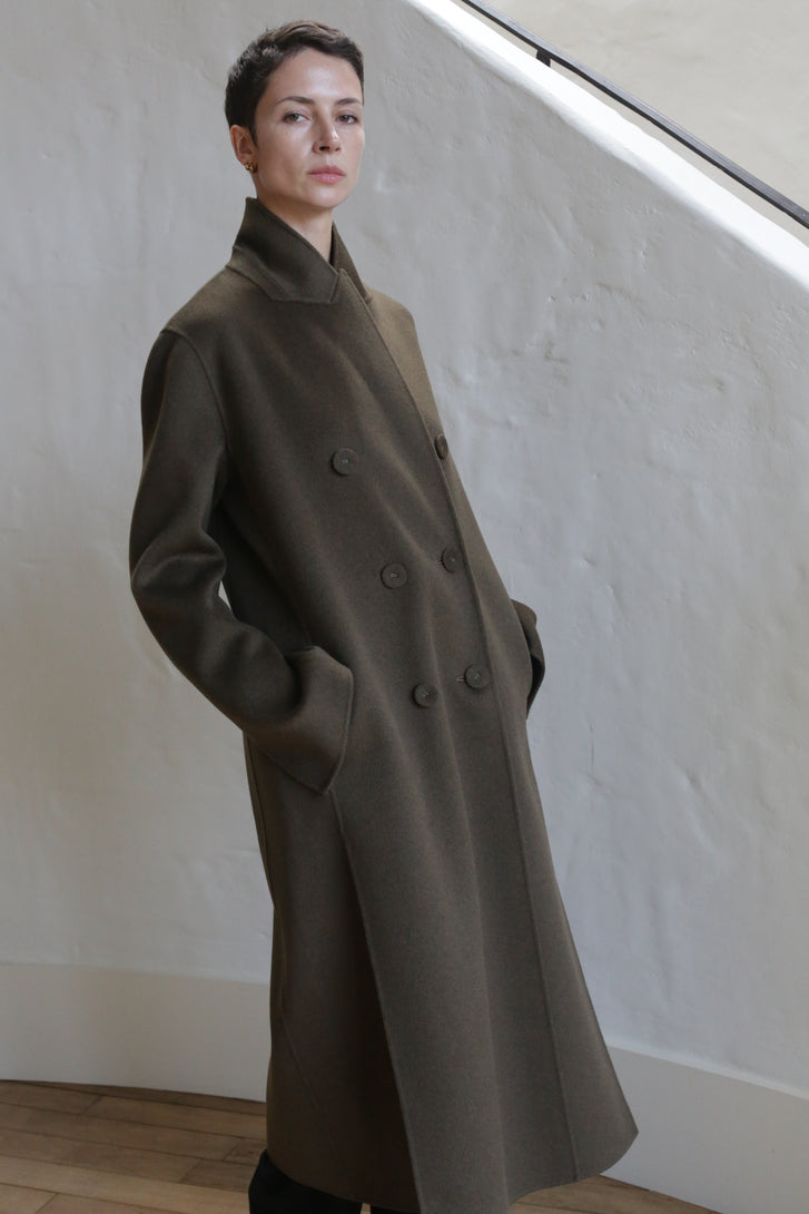 A person wearing the Doublebreasted Coat in Olive.