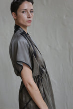 Load image into Gallery viewer, A person with short dark hair and gold earrings wears the Lune Dress | Butterfly Wing, a gray and black short-sleeved dress, standing sideways and looking at the camera against a light-colored wall.
