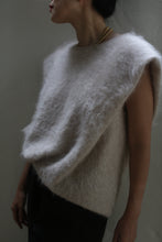 Load image into Gallery viewer, A person is wearing the Salento | Sandstone, a sleeveless, light-colored, fuzzy sweater crafted from brushed cashmere. They are posing against a dark, minimalist background. Only their upper torso is visible, revealing dark pants and a hint of a gold necklace.