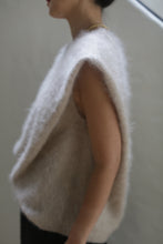 Load image into Gallery viewer, A person is shown from the side wearing the Salento | Sandstone, a sleeveless, fluffy light beige luxurious vest, against a plain background. The individual has short dark hair and wears a beaded necklace. The image captures only the upper body and part of the arm.