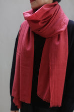 Load image into Gallery viewer, Person wearing a vibrant coral cashmere scarf wrapped snugly around their neck over a black top. The image focuses on the 100% woven Tissue Weight Cashmere Scarf and torso, with the person&#39;s face partially visible. The background is neutral and blurry, keeping the attention on the luxurious clothing.