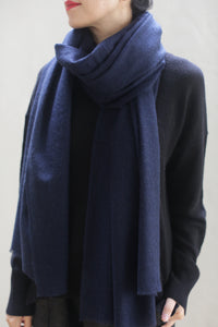 A person wearing a dark blue Tissue Weight Cashmere Scarf in Navy and a black sweater. Only the lower half of their face and upper torso are visible against a light-colored background. Their dark hair is pulled back, and their arms are relaxed by their sides.