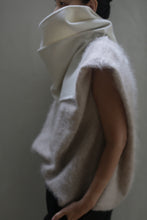 Load image into Gallery viewer, A person is wearing the Wrap Scarf | Undyed, a soft and fuzzy accessory made from double-faced cashmere with a high, structured collar that covers part of their face. The neutral colors create a soft, minimalistic look. The plain background draws attention to the elegant zero-waste design of the clothing.