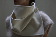 Load image into Gallery viewer, A person is wearing the stylish Wrap Scarf in off-white, made of undyed double-face cashmere, with a high collar that is artistically folded and accented with a button detail. Layered over it is a soft, fuzzy grey top. The background is a muted, solid color.