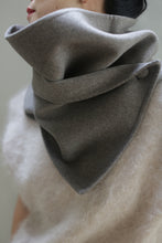 Load image into Gallery viewer, Close-up of a person wearing the Wrap Scarf | Undyed Natural, made from double-face cashmere and wrapped around their neck, covering the lower half of their face. This handmade scarf from Atelier Lan Janicke is paired with a textured, fluffy white sweater. The background features a muted, soft green tone.