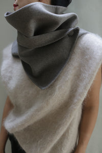 A person is wearing a large, textured, off-white Wrap Scarf | Undyed Natural from Atelier Lan Janicke around their neck. The scarf is partly covering their face and the background features a light, neutral color. Both pieces are handmade using undyed double-face cashmere for a zero waste design.