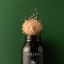 Load image into Gallery viewer, A dark glass jar of Healing Spirit Soak salt scrub, enriched with Pink Himalayan salts, is set against a solid green background. The jar&#39;s black label features white text and a floral design. The scrub is heaped on top of the open jar, spilling slightly onto the background.