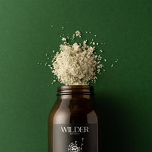 Load image into Gallery viewer, A dark brown glass jar labeled &quot;Herbal Tranquility Soak&quot; by Wilder Botanics is seen against a green background. The jar is open, with a heap of coarse white Epsom salts spilling out from the top. The arrangement is minimalistic and visually striking.