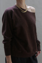 Load image into Gallery viewer, A person wearing the Ballerina&#39;s Cashmere Sweater in chestnut, an off-the-shoulder piece that serves as a classic wardrobe staple, paired with a gold chain necklace. The background is neutral gray, offering a minimalistic appearance. The individual&#39;s face is not visible in the image.