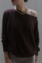 Load image into Gallery viewer, Against a neutral background, a person is wearing the Ballerina&#39;s Cashmere Sweater in Chestnut, featuring a loose fit and stylish boat neck that elegantly exposes one shoulder. They have accessorized with a gold chain necklace and their lips are painted red. This cashmere sweater is undoubtedly a wardrobe essential.