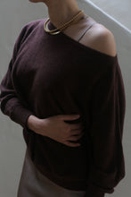 Load image into Gallery viewer, A person wearing the Ballerina&#39;s Cashmere Sweater in Chestnut, which is a loose-fitting, off-the-shoulder wardrobe staple, and a gold necklace. They stand against a neutral background with one hand across their midsection.