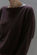 Load image into Gallery viewer, The image showcases a person wearing a Ballerina&#39;s Cashmere Sweater in Chestnut featuring a boat neck, complemented by a gold necklace. The focus is on the upper body and the sweater&#39;s luxurious texture, enhanced by soft lighting. The backdrop is a muted gray.