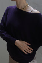 Load image into Gallery viewer, A person wearing the Ballerina&#39;s Cashmere Sweater in Aubergine, a true wardrobe staple, and a gold necklace is shown from the neck down, posing with one hand on their stomach against a plain background.