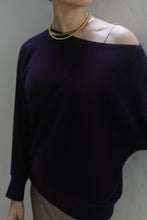 Load image into Gallery viewer, A person is wearing a Ballerina&#39;s Cashmere Sweater in aubergine, revealing a beige strap underneath, paired with a gold bead necklace. The background is a neutral gray wall, highlighting this wardrobe staple.