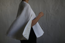 Load image into Gallery viewer, A person dressed in black is wearing a wide-sleeved, white &quot;Capelet Long&quot; made from Japanese Wool Gauze Undyed. The custom-made item is displayed from the shoulders to the waist against a light gray textured background. The capelet billows slightly, adding a sense of movement and elegance. This made-to-order piece has a completion time of 3-4 weeks.