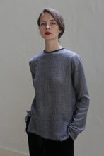Load image into Gallery viewer, A person with short brown hair, wearing a Crewneck shirt - Japanese Wool Gauze | BW Houndstooth in gray, stands against a plain, light-colored background. The individual gazes at the camera with a neutral expression, hands partially in the pockets of dark pants. The shirt&#39;s Japanese wool gauze adds a touch of sustainable design to the overall look.