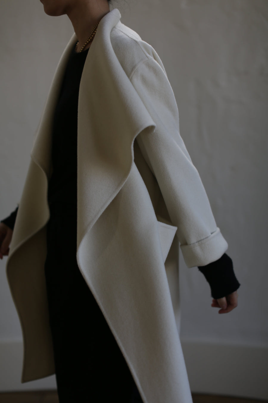 A person wearing an unbuttoned, draped-collar Winston Long Double-face | Undyed coat in undyed cashmere over a black outfit.