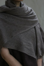 Load image into Gallery viewer, A person wears a Tissue Weight Cashmere Scarf in taupe, the soft woven fabric draped loosely around their shoulders. Their face is partially visible against a plain, neutral background.